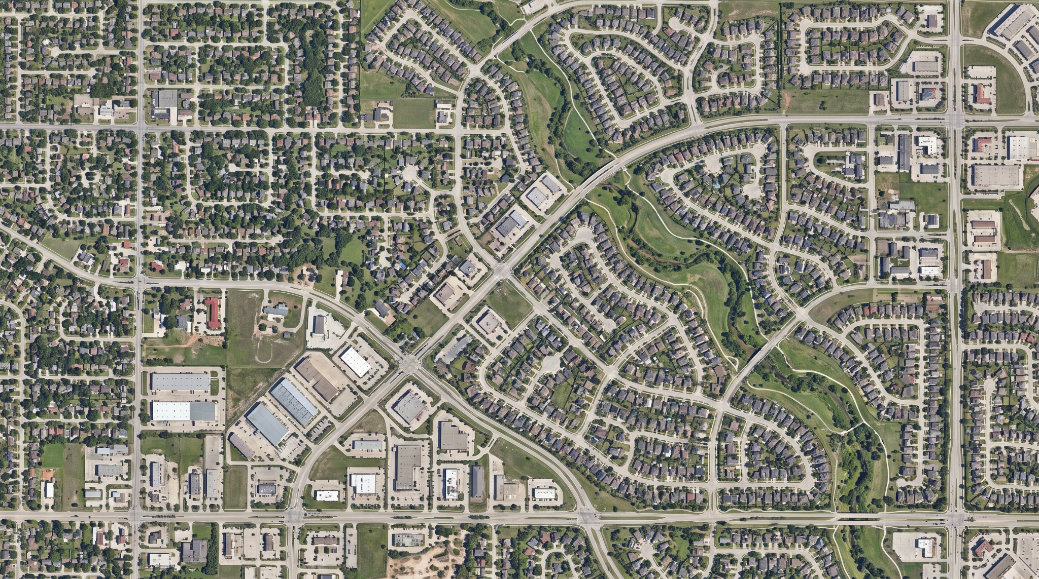 Overhead view of a broad suburban service territory with residential neighborhoods, commercial areas, connecting roads, and a central greenbelt.